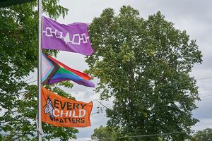 Photo of the Iroquois Confederacy Flag, a Pride Flag, and an Every Child Matters Flag on a flag pole.