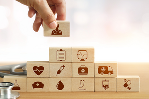 hand building a pyramid of children's toy wooden building blocks. One each wooden block there is a health care related icon.